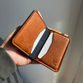 Brown leather wallet with card slots held in a hand against a neutral background