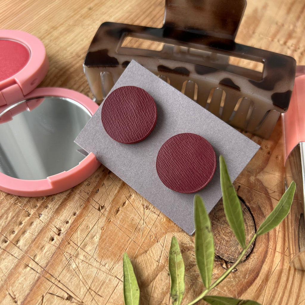 Red circular earrings on a card with a hair clip and compact mirror on a wooden surface.
