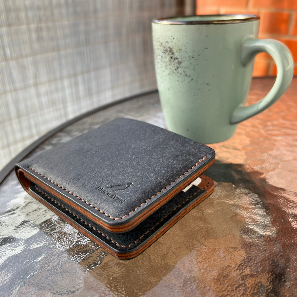 Black wallet on a glass table with a green mug in the background